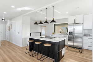 Kitchen featuring white cabinets, stainless steel refrigerator with ice dispenser, hanging light fixtures, a kitchen bar, and dark cabinets