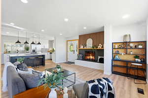 Living room featuring light wood-type flooring, a warm lit fireplace, and recessed lighting