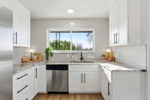 Kitchen with stainless steel appliances, white cabinets, light wood-style flooring, recessed lighting, and light stone countertops