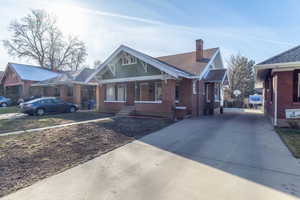 Bungalow-style home with a chimney, brick siding, a porch, driveway, and roof with shingles