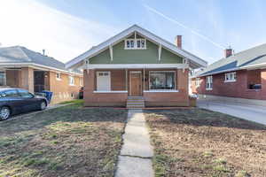 Bungalow-style home with a chimney, a porch, brick siding, and a front yard