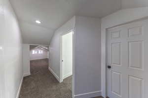 Corridor featuring lofted ceiling, dark carpet, and a textured ceiling