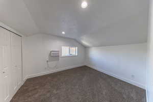 Additional living space with a textured ceiling, lofted ceiling, dark colored carpet, and recessed lighting