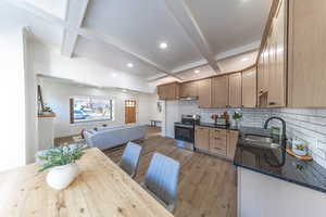 Kitchen featuring light wood finished floors, dark stone counters, stainless steel electric stove, open floor plan, and beam ceiling