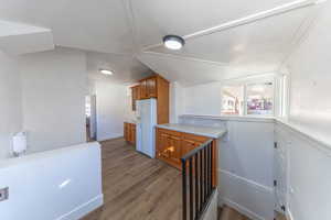 Kitchen featuring brown cabinets, vaulted ceiling, white fridge with ice dispenser, light countertops, and dark wood-type flooring