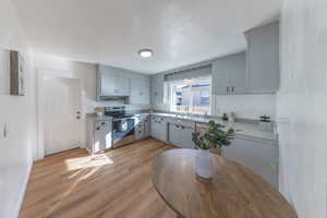 Kitchen featuring light countertops, stainless steel electric stove, gray cabinets, and light wood finished floors