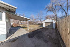 Fenced yard with an outdoor structure, a detached garage, asphalt driveway, and a patio area