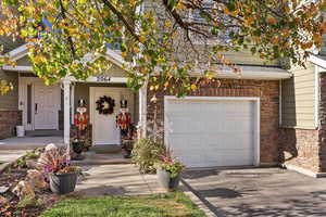 Doorway to property featuring stone siding, an attached garage, a porch, and driveway