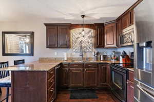 Kitchen with dark brown cabinets, a breakfast bar area, stainless steel appliances, light stone counters, and a textured ceiling