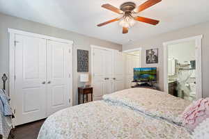Bedroom with multiple closets, dark wood-type flooring, a ceiling fan, and connected bathroom