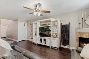Living room featuring dark wood-type flooring, ceiling fan, and a tile fireplace
