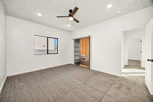 Unfurnished bedroom featuring light carpet, ceiling fan, recessed lighting, and a barn door