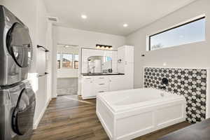 Full bath featuring vanity, a bath, stacked washer and clothes dryer, dark wood-type flooring, and recessed lighting