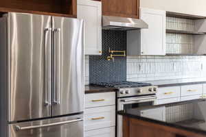 Kitchen featuring open shelves, appliances with stainless steel finishes, white cabinets, ventilation hood, and backsplash