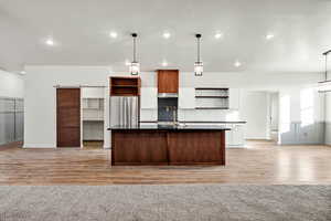 Kitchen featuring open shelves, a barn door, a kitchen island with sink, open floor plan, and recessed lighting