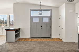 Entrance foyer featuring vaulted ceiling, a chandelier, light wood-type flooring, and light colored carpet
