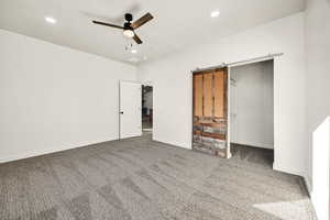 Unfurnished bedroom with carpet flooring, a ceiling fan, recessed lighting, a barn door, and a spacious closet