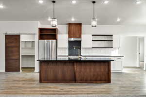 Kitchen with open shelves, white cabinets, pendant lighting, a barn door, and a kitchen island with sink