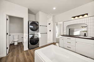 Full bath featuring vanity, dark wood-style flooring, a bath, and estacked washer and dryer