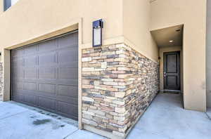 Entrance to property featuring stone siding, a garage, and stucco siding