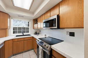 Kitchen with brown cabinets, tile counters, appliances with stainless steel finishes, and decorative backsplash