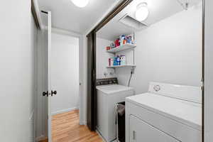 Washroom with light wood-type flooring and washing machine and clothes dryer