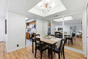 Dining area with a chandelier, light wood-style floors, a skylight, and a tray ceiling