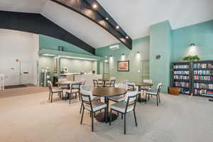 Carpeted dining area with high vaulted ceiling and beamed ceiling