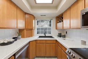 Kitchen with tile counters, appliances with stainless steel finishes, tasteful backsplash, and brown cabinetry