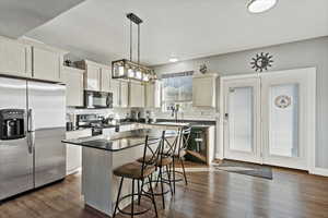 Kitchen featuring black appliances, a kitchen bar, backsplash, decorative light fixtures, and a kitchen island