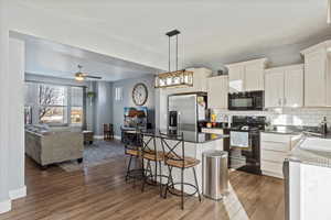Kitchen with black appliances, a breakfast bar, hanging light fixtures, dark stone counters, and ceiling fan