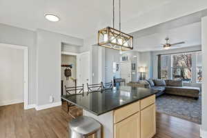 Kitchen with light brown cabinets, dark stone counters, a kitchen bar, and dark wood-type flooring