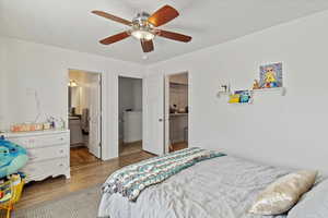 Bedroom featuring light wood-type flooring, a spacious closet, a ceiling fan, and ensuite bath