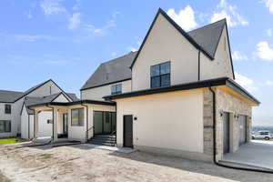 Rear view of house with stucco siding, stone siding, a garage, and roof with shingles