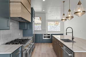 Kitchen featuring light stone countertops, appliances with stainless steel finishes, decorative backsplash, a center island with sink, and light wood-style flooring