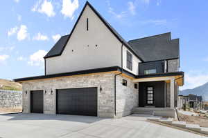View of front of home with stone siding, concrete driveway, a shingled roof, and stucco siding