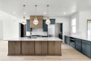 Kitchen with light stone countertops, a center island with sink, tasteful backsplash, blue cabinetry, and recessed lighting
