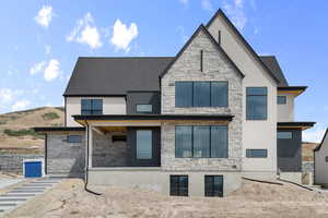 Rear view of property with stone siding, a shingled roof, and a patio