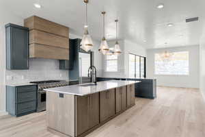 Kitchen featuring a center island with sink, light stone countertops, pendant lighting, high end stove, and light wood-type flooring