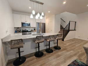Kitchen featuring a kitchen breakfast bar, stainless steel appliances, light stone countertops, white cabinetry, and hanging light fixtures