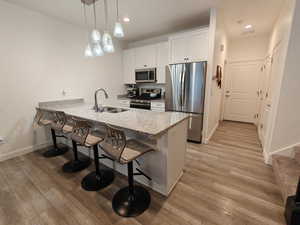 Kitchen with a kitchen breakfast bar, light stone counters, stainless steel appliances, a peninsula, and light wood-style flooring