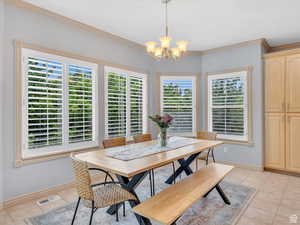Dining area with ornamental molding, light tile patterned floors, and a chandelier