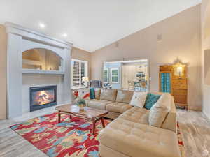 Living area with light wood finished floors, a tile fireplace, high vaulted ceiling, and recessed lighting