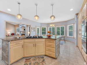 Kitchen featuring light brown cabinetry, a warm lit fireplace, a center island, dark stone countertops, and recessed lighting
