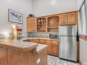 Kitchen featuring appliances with stainless steel finishes, a peninsula, open shelves, and brown cabinetry