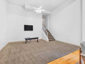 Unfurnished living room with ceiling fan, carpet floors, wood finished floors, and stairway