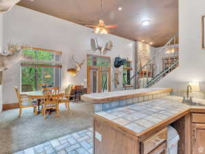 Kitchen featuring a peninsula, a ceiling fan, brown cabinetry, light carpet, and tile counters
