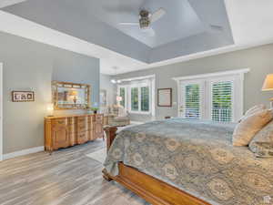 Bedroom with access to outside, light wood-style flooring, a tray ceiling, ceiling fan, and a chandelier