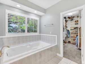 Bathroom with a walk in closet, light colored carpet, light tile patterned floors, a garden tub, and recessed lighting