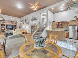Dining room featuring ceiling fan, stairs, light colored carpet, bar with sink, and light stone finish floors